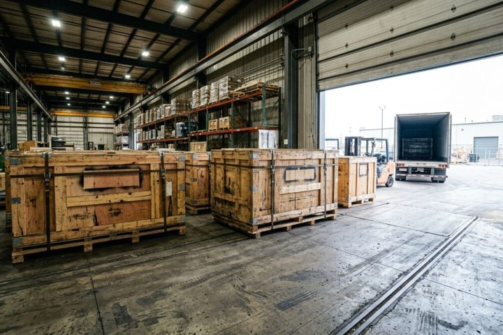 Crated converting machinery in a receiving bay, heavy timber crates with steel banding and blank stencil panels, roller...